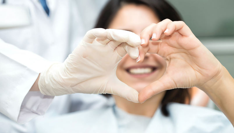 A smiling woman at a dental clinic in London, Ontario, with her dentist forming a heart shape with gloved hands.